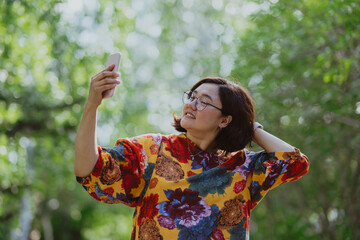 Cheerful young lady with glasses capturing a selfie in a lush green park. Young entrepreneur with digital devices capturing a selfie, staying connected in an urban green space