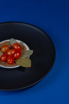 Tomate cereja em prato preto e fundo azul escuro