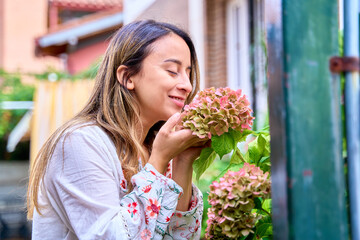 young Caucasian woman smelling a large flower with a smile on her face and eyes closed