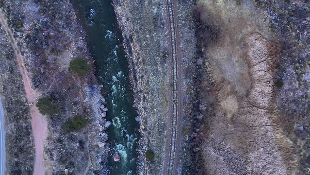 Vertical overhead drone shot of river rapids parallel to train tracks at dawn in C