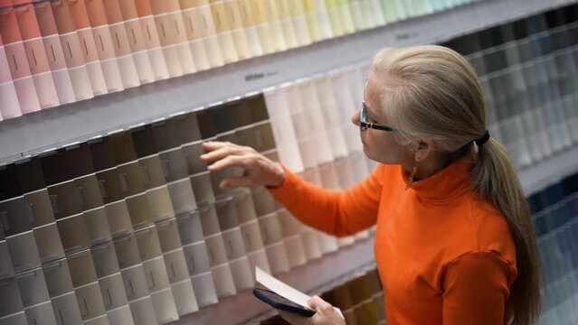 Slow motion closeup of mature woman using phone looking at paint chips in a hardware store. Concept of shopping experience for home improvement.