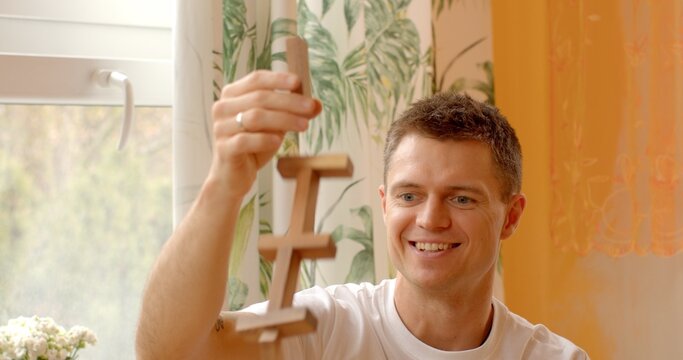 Wooden block structure collapsed while attempting to build another level upwards. Man smiles, displaying a lighthearted attitude towards failures, young man embraces setbacks as part of the process.