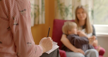 Woman with a child, hand in the foreground writing something on a piece of paper. Case worker or social worker meeting with client to discuss services, assistance, support provided by social services.