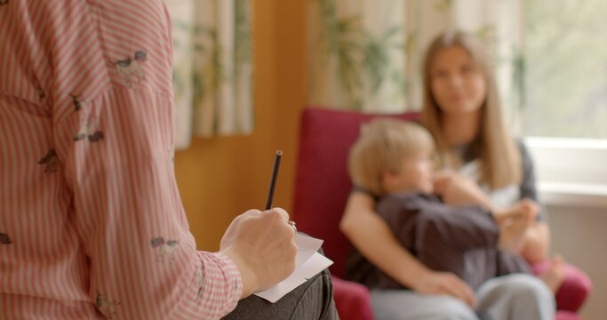 Woman with a child, hand in the foreground writing something on a piece of paper. Case worker or social worker meeting with client to discuss services, assistance, support provided by social services.