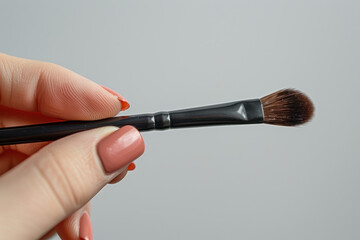 Hand holding make-up brush cosmetic isolated on gray