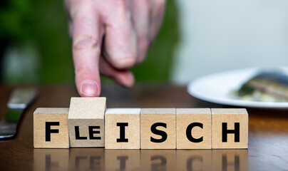 Hand turns cube and changes the German word 'Fleisch' (meat) to 'Fisch' (fish). Symbol for eating more healthy and choosing fish instead of meat.