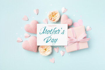 Festive background for Mothers Day. Paper card, hearts, rose flowers and gift box on blue table top view. - 781382449