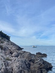 View of boat from an island with rocky outcrop and blue sea and clear sky