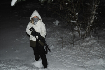 Rebel girl in winter camouflage and with a rifle in her hand in the forest at night.
