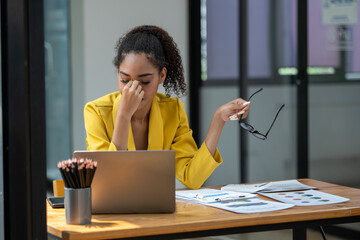 Distressed young businesswoman feeling pressure and headache at her office desk with laptop and...