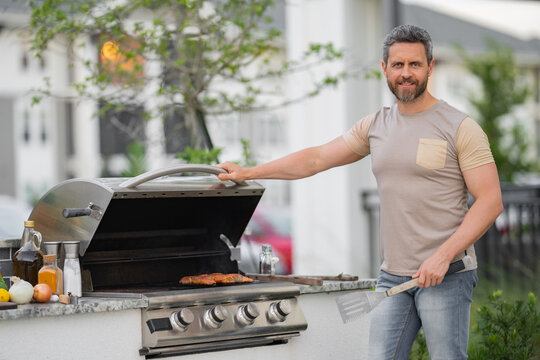 Cropped image of handsome man is making grill barbecue outdoors on the backyard. Bbq party. Bbq meat, grill for picnic. Roasted on barbecue. Man preparing barbeque in the house yard.