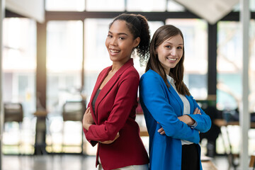 Two diverse businesswomen standing back-to-back, projecting confidence and partnership in a modern office space.