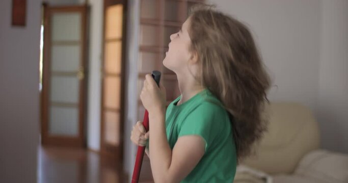 Creative Teenage Girl Singing and Using Broom Handle as Microphone. Child Using Mop as Microphone While Singing in Domestic Room. Enjoying Home Cleaning. Playful Creative Kid Dancing With Mop.