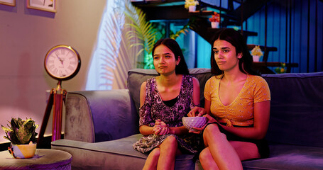 Indian Asian teen age female pair sitting sofa couch watch late night enjoy fun joy sad movie film...
