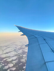 Fototapeta premium View from airplane window. Wing of an aircraft. Aerial view of blue sky and clouds. The white wing of the plane at sunrise.
