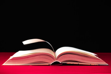 Pages of a thick book are turned on a pink and black background, space for text.