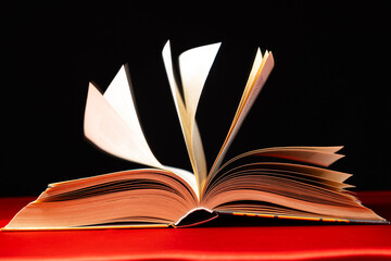 Pages of a thick book are turned on a red and black background.