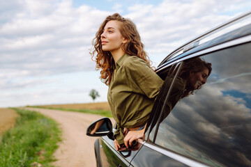 Pretty woman resting and enjoying travel out of the car window. Lifestyle, weekend, tourism, nature, active life.