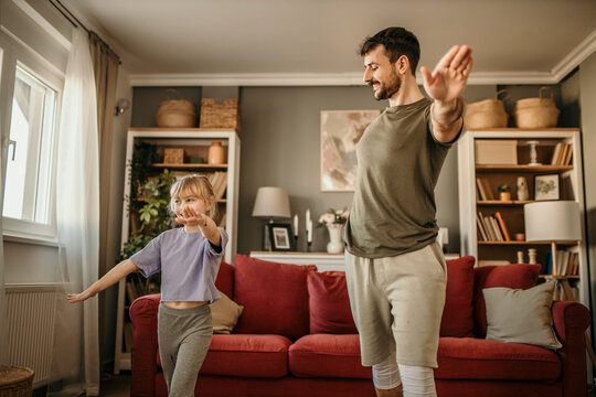 Father and daughter dressed in sporty attire, laughing and working out in their sunny, modern living room