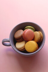 Purple cup filled with pastel macarons on pink background. Selective focus.