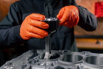 close-up At a service station on the table young engine repairman puts a piston part in place