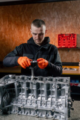 At a service station on the table young engine repairman puts a piston part in place