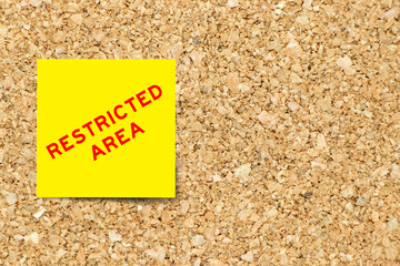 Yellow note paper with word restricted area on cork board background with copy space
