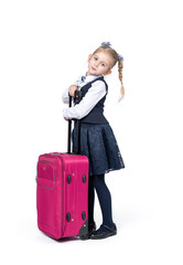 A happy little girl in a school uniform stands with a large pink suitcase, isolated on a white background
