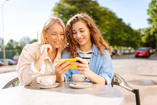 Two young women sitting in the cafe, enjoying in coffee and having fun with smartphone. Coffee break after shopping. Fashion, beauty, blogging, tourism.