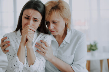 Confident worried mature mother embracing and helping sad daughter with broken heart, family support, mid aged mom soothe crying adult child, divorce or miscarriage, share problem with someone close - 781407890