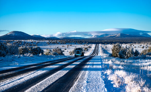 Frozen highway from Grand Canyon National Park to Williams Arizona on a cold sunny winter morning. Snow covered lanes in wide american landscape with oncoming truck. Calm atmosphere with blue sky.