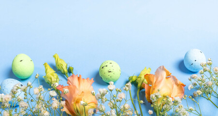 Pastel decorative eggs, delicate fresh flowers on light blue backdrop. Holiday Easter card template.