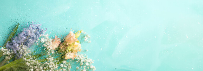 Banner for spring holiday. Blurred flowers on turquoise. Shot through wet glass. Copy space.