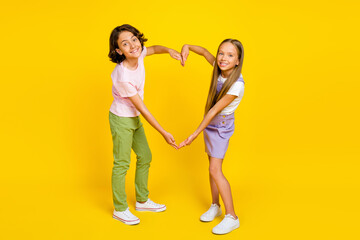Full length photo of sweet positive friends wear casual outfits showing arms big heart isolated yellow color background