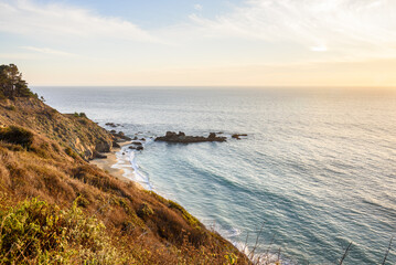 Small sandy beach at the foot of a grassy cliff along the coast of central California at sunset in autumn
