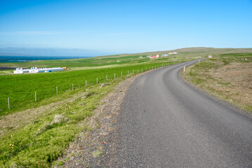 Fototapeta na wymiar Desertefd back road through a rural landscape with grassy fields and farm buildings in Iceland on a sunny summer day