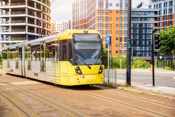 Yellow tram on a tramway running through a new suburban residental district on a sunny summer day. An apartment building under construction is in background. - obrazy, fototapety, plakaty