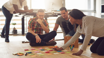 Creative people looking at post-it notes laid out on floor. Mixed race business associates...