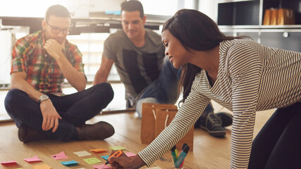 Creative people looking at post-it notes laid out on floor. Mixed race business associates...