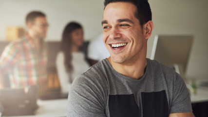 Cheerful creative businessman standing with arms crossed. While his three diverse colleagues are in the background talking together