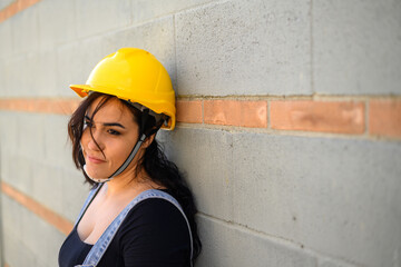 Hispanic woman work in construction site wear yellow hard hat and gloves blue jeans overall outdoors