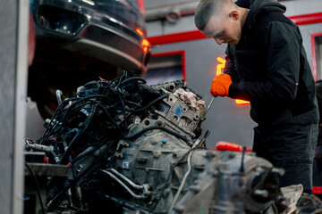 Fototapeta premium At a service station young master repairs a motor part removed from a car for a complete overhaul