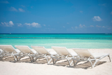 The row of empty sun loungers on a beautiful tropical beach with white sand and turquoise sea water without people. The best summer vacations ideas and destinations. Caribbean copy space background 