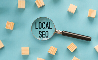 Magnifying glass loupe with sign LOCAL SEO between and wooden cubes on the blue table.