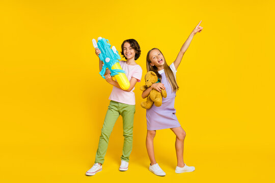 Full length photo of dreamy funky friends wear casual outfits playing toys pointing emtpy space isolated yellow color background