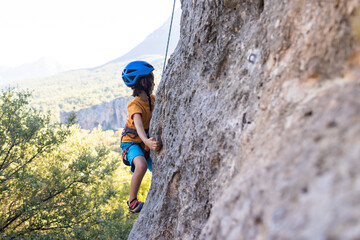 Children's rock climbing. The boy climbs a rock against the backdrop of mountains. Extreme hobby. An athletic child trains to be strong. - 781425873