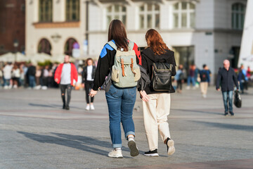 A pair of Gen Z student friends with backpacks stroll through a busy city square. Their style and friendship shine against the urban backdrop, representing modern youth and freedom of relationships