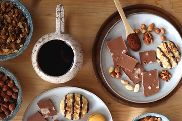 Cup of tea or coffee, cookies, macaroons, chocolate, various nuts and cocoa powder on wooden table....