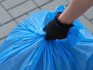 A close-up shot of a person hand taking a blue garbage bag full of trash
