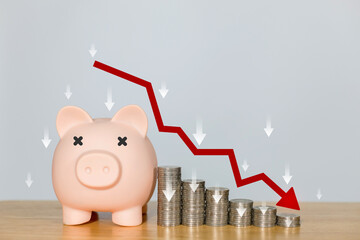 Piggy bank upside down with coins stack and down arrow graph represents the financial crisis....